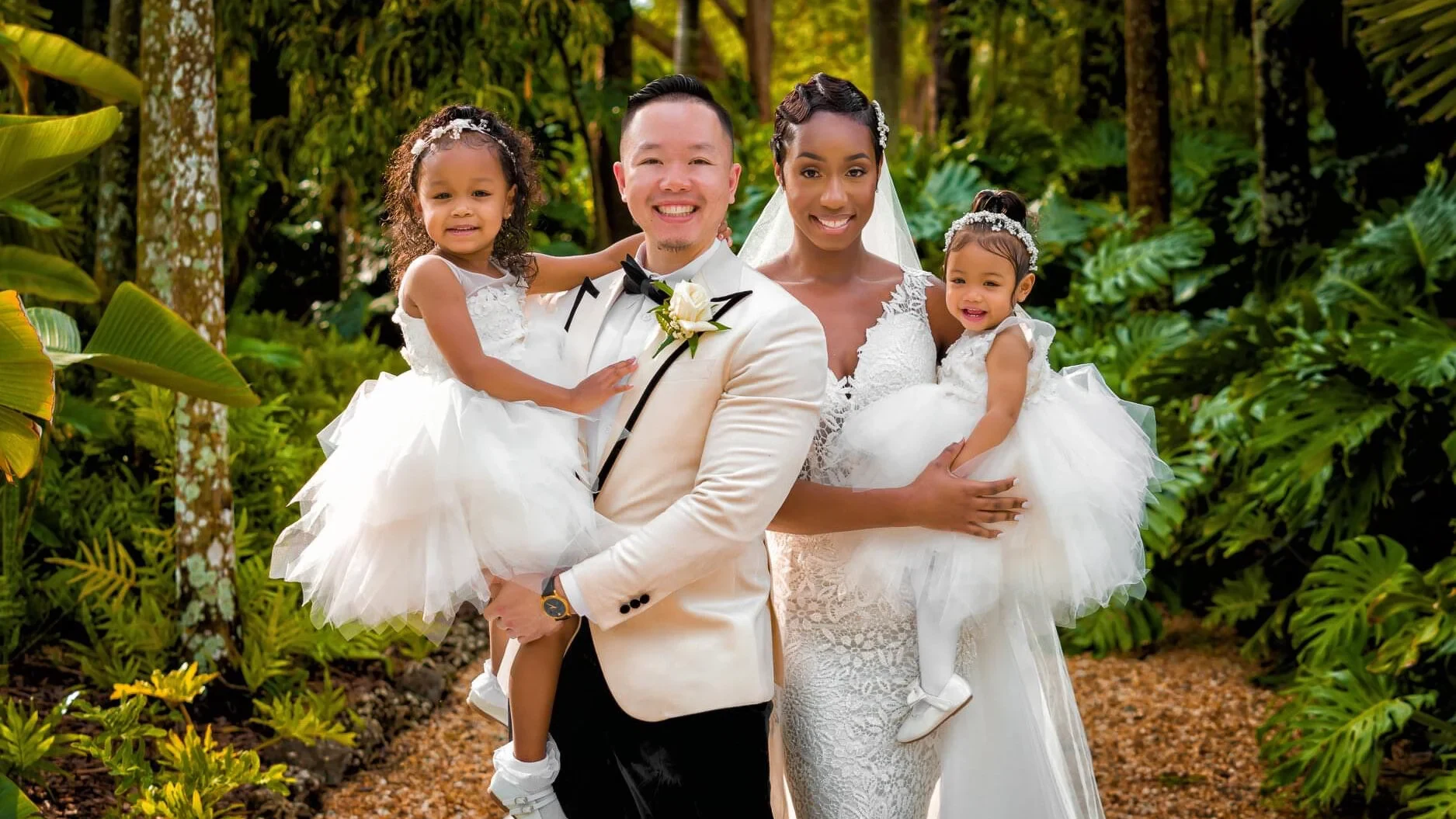 The newlyweds holding their two young daughters in a tropical garden.