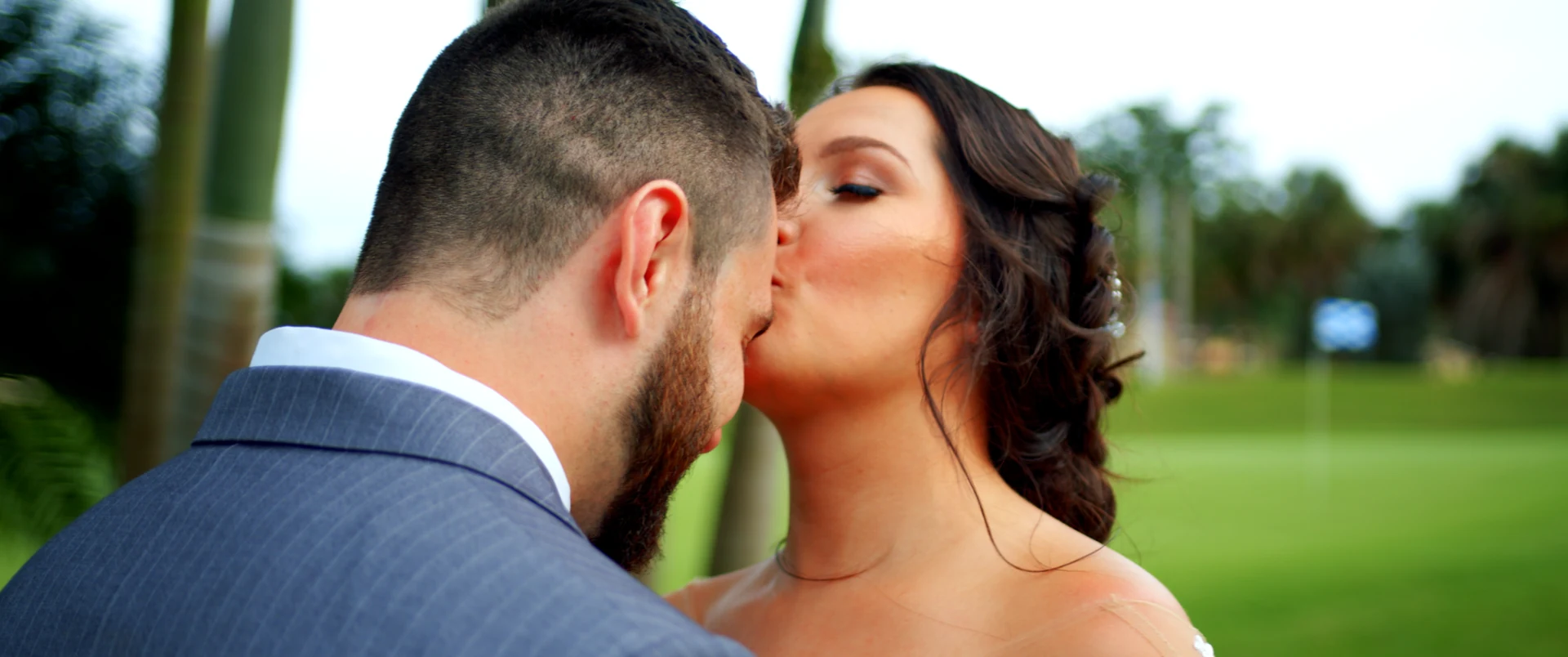 A bride kisses her groom on the cheek in a green garden.